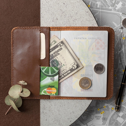 Whiskey brown leather passport cover open with a passport, banknote, card and coins on a stone surface