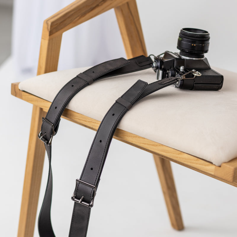 Black leather camera strap draped over a wooden chair with a vintage camera