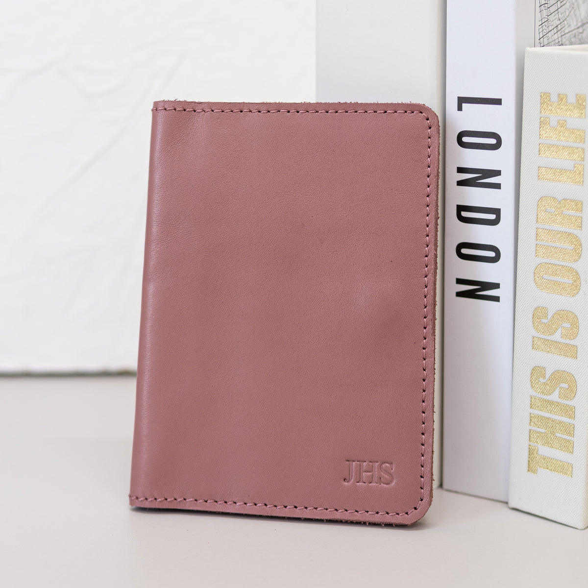 Closed pink leather passport wallet standing against a London book