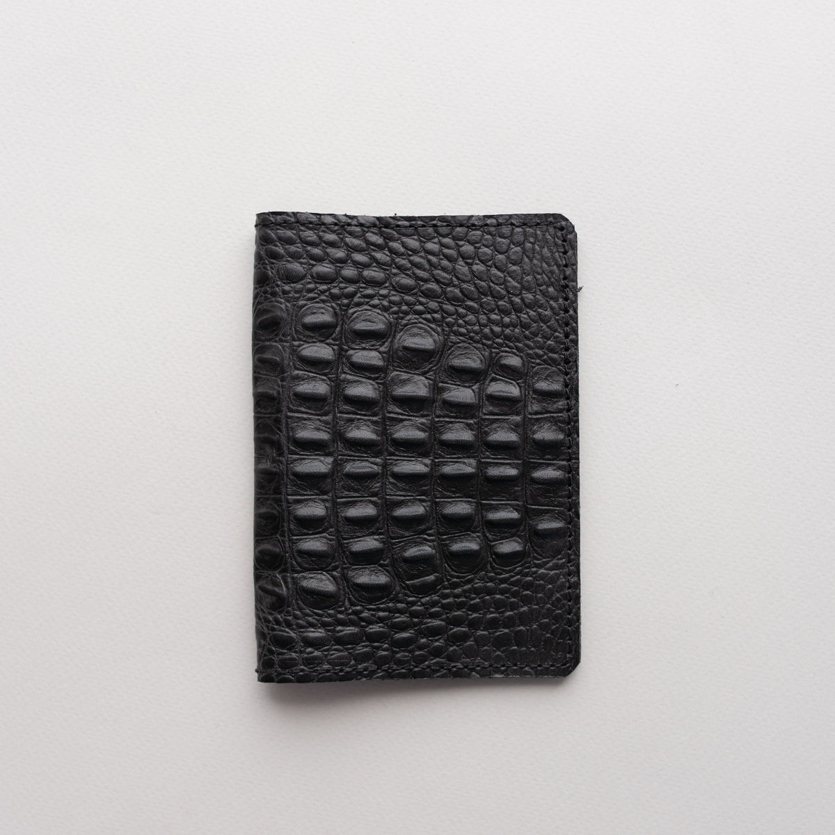 Black crocodile-embossed leather passport cover on a light background