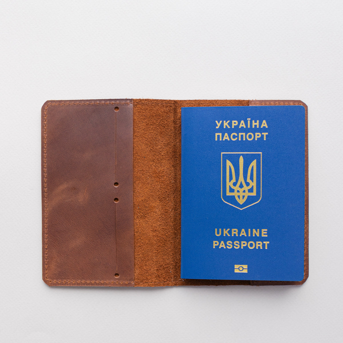 Open whiskey brown leather passport cover with a passport on a grey surface